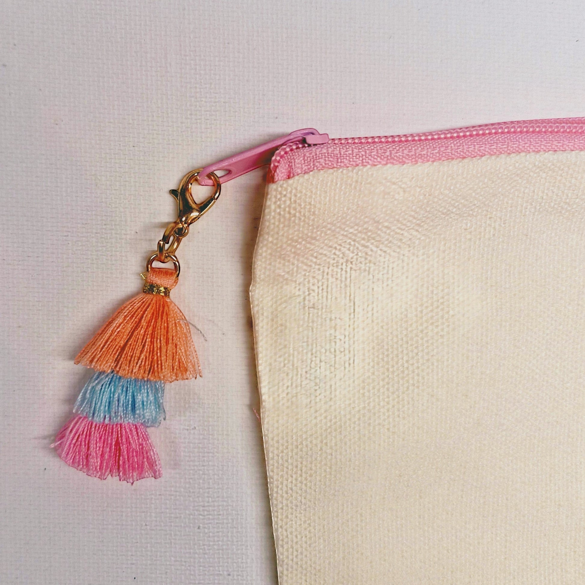 Pochette Femmes de pilotes en lin écru avec pompons dégradés orange, bleu et rose, fermeture éclair rose.