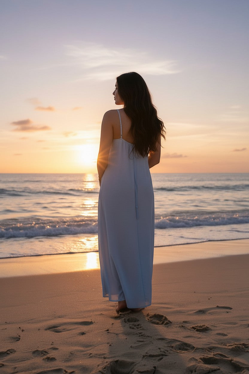 Femmes de pilotes robe longue bleu pâle fluide avec bretelles ajustables, portée par une femme sur une plage au coucher du soleil.